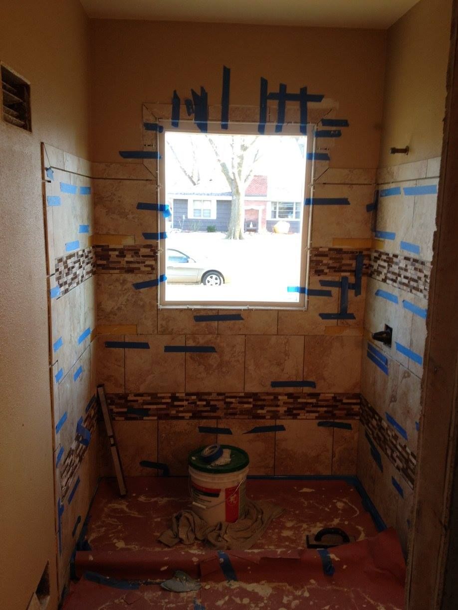 Small tiled bathroom under renovation with blue tape, a window, and a bucket on the floor.