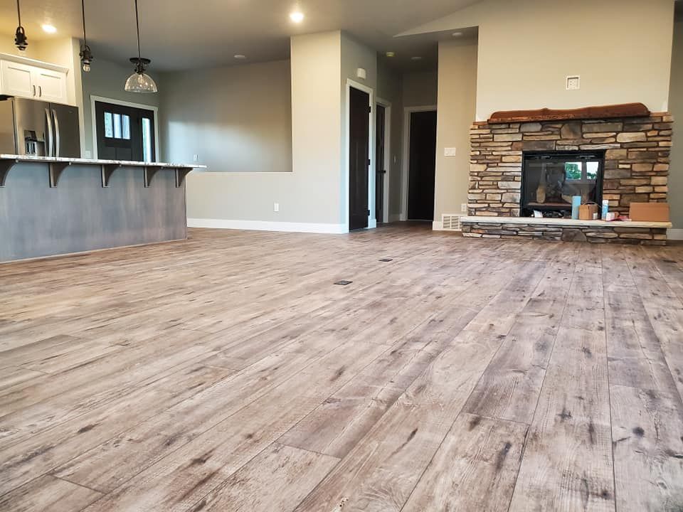 Empty open-plan living room with wood-look floors, gray walls, kitchen bar, and stone fireplace.