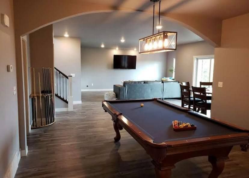 Spacious basement game room with a pool table, wall TV, chandelier, and dining table in the back.
