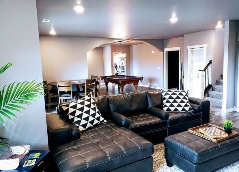 Modern living room with black leather sectional, patterned pillows, and arched doorway to dining area
