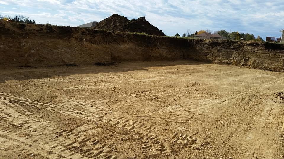 Wide dirt excavation site with leveled ground, steep earthen walls, and a cloudy sky overhead