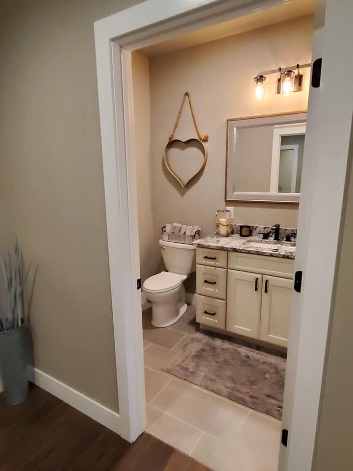 Small bathroom with toilet, vanity, mirror, heart wall decor, and beige tile floor.