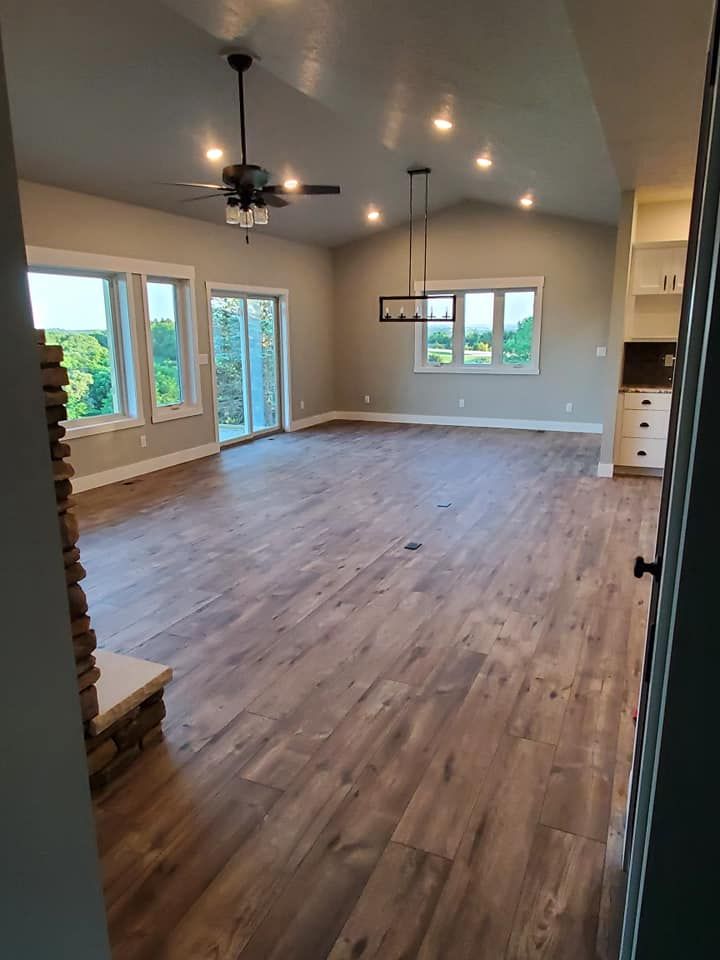 Spacious empty living room with wood floors, ceiling fan, recessed lights, and large windows with a view outside.