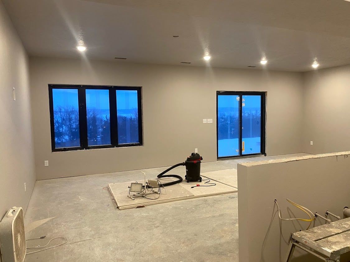 Unfinished living room with gray walls, recessed lights, blue-tinted windows, and construction materials on the floor