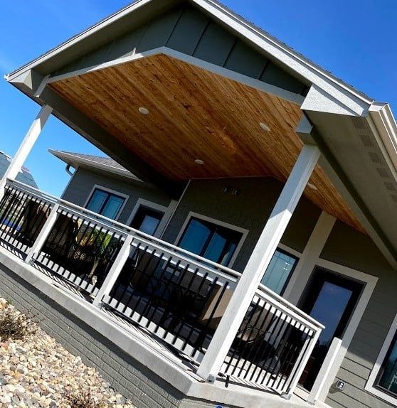 Modern house porch with white columns, black railing, and a wood-paneled ceiling under a blue sky