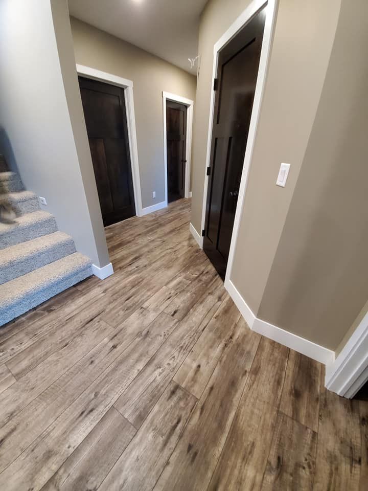 Hallway with wood-look flooring, beige walls, dark doors, and carpeted stairs on the left.