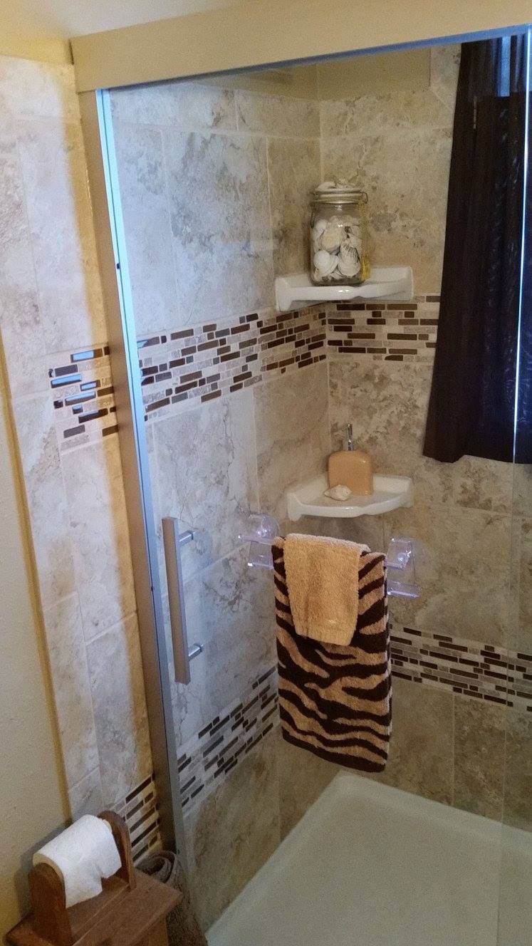 Small tiled shower with glass door, built-in shelves, and a zebra-striped towel hanging on the wall.