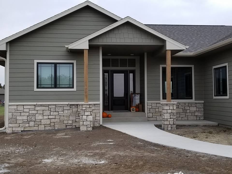 Front view of a new gray house with stone base, covered porch, and curved concrete walkway.