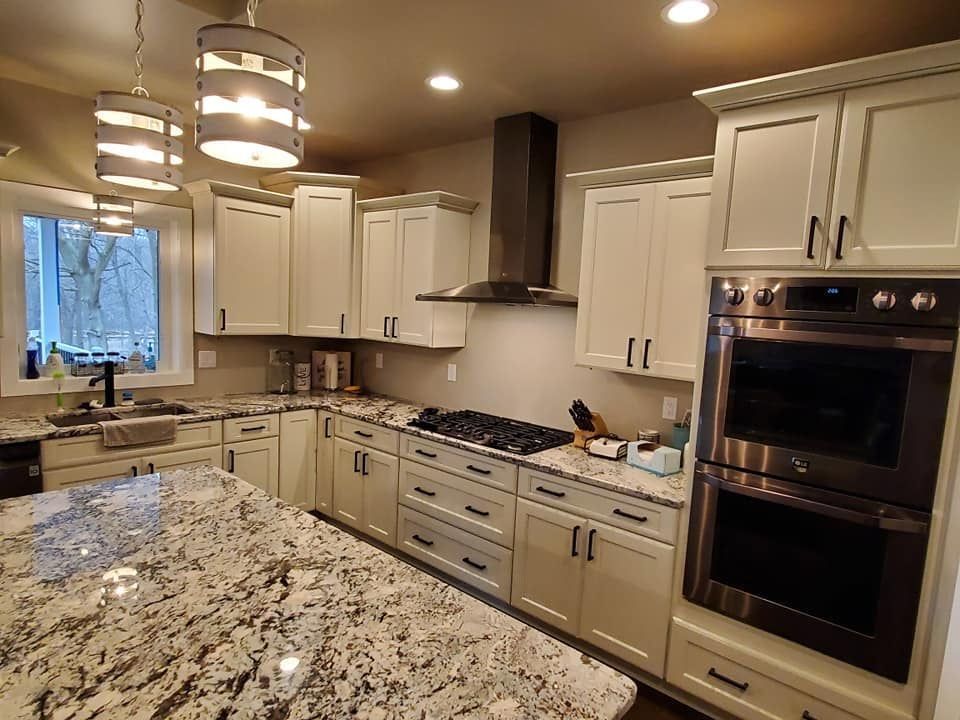 Modern kitchen with white cabinets, granite island, stainless steel appliances, and pendant lighting.