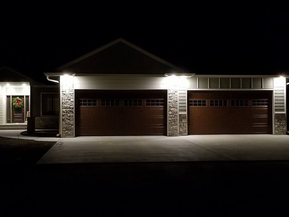 Nighttime view of a well-lit suburban house with two garage doors and a front porch.