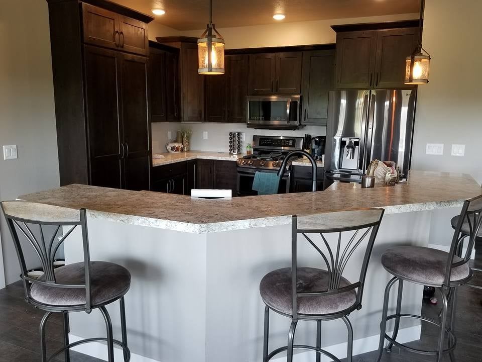 Modern kitchen with dark cabinets, stainless steel appliances, and a curved stone breakfast bar with stools