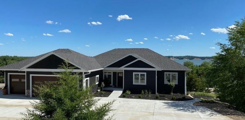 Dark blue single-story house with attached garage, gravel driveway, and mountain view under a clear sky