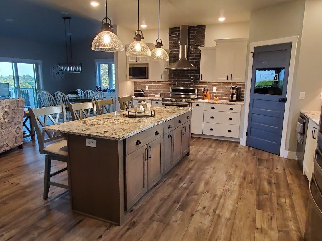 Modern kitchen with a large granite island, pendant lights, wood floors, and a blue pantry door.