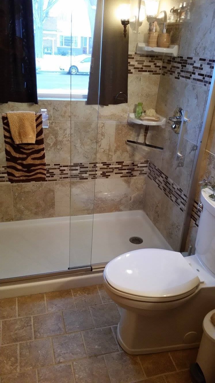 Small bathroom with a bathtub-shower combo, toilet, tiled walls, and a window with curtains.