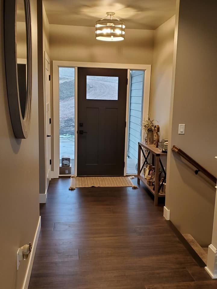 Narrow hallway with wood floor leading to a front door, lit by a ceiling fixture, with a side console table.