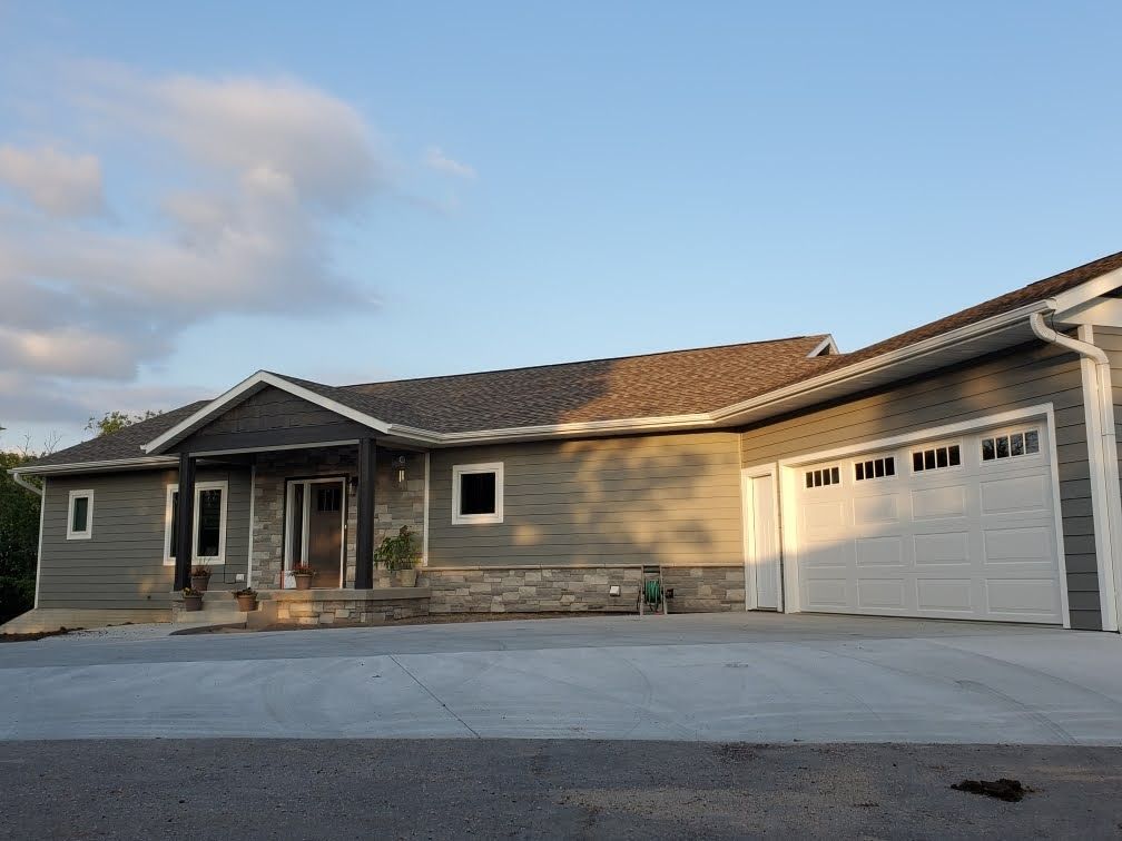 Single-story beige house with stone facade and attached white garage at sunset