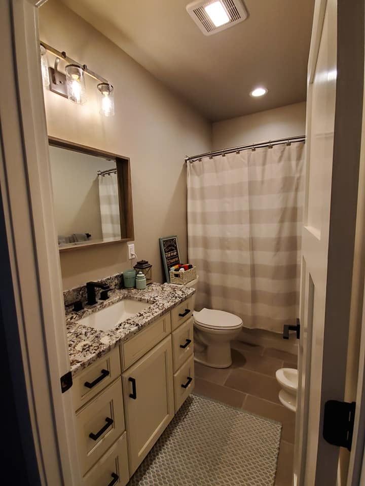 Compact bathroom with granite vanity, mirror, toilet, shower curtain, and patterned floor rug.