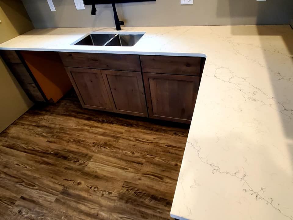 Kitchen with white countertop, double sink, wood cabinets, and dark wood flooring.