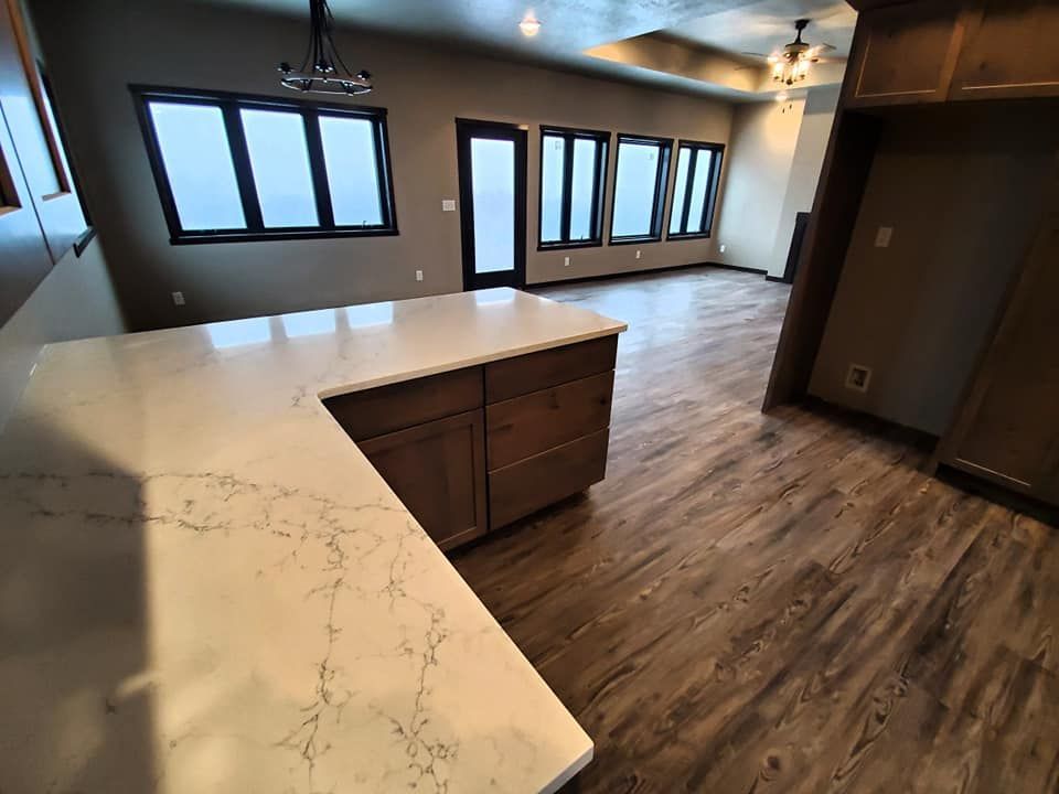 Empty modern kitchen with L-shaped white countertop, wood cabinets, and large windows
