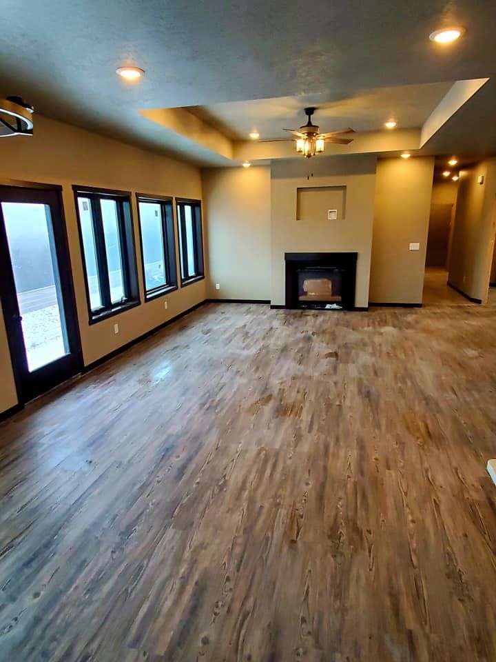Empty living room with wood floors, recessed lights, large windows, a ceiling fan, and a fireplace.