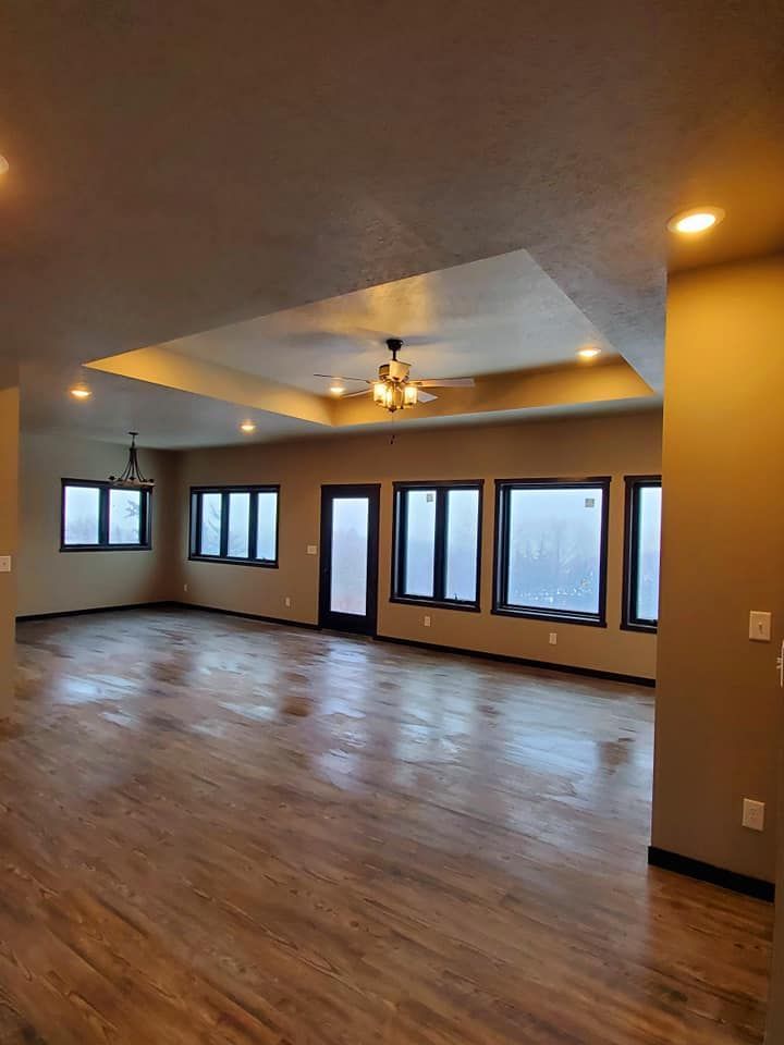 Empty living room with hardwood floors, beige walls, recessed lights, and multiple windows overlooking a foggy view