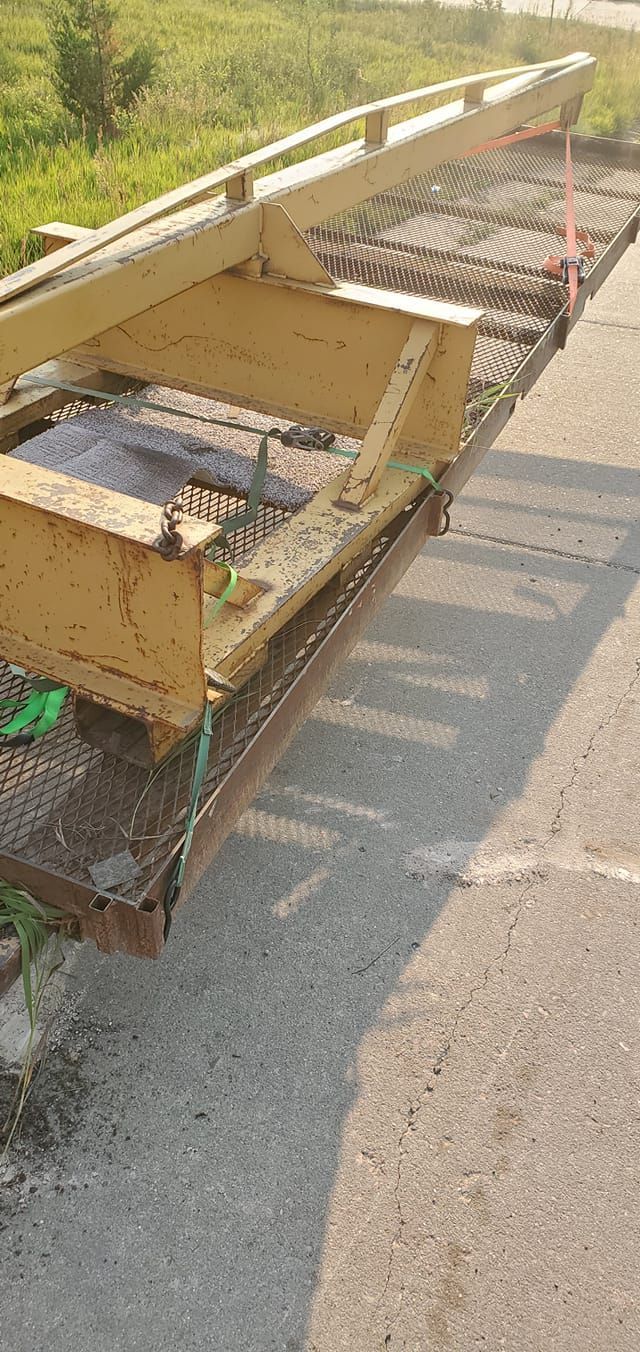 Damaged yellow roadside barrier and metal debris lying along a sunlit paved road