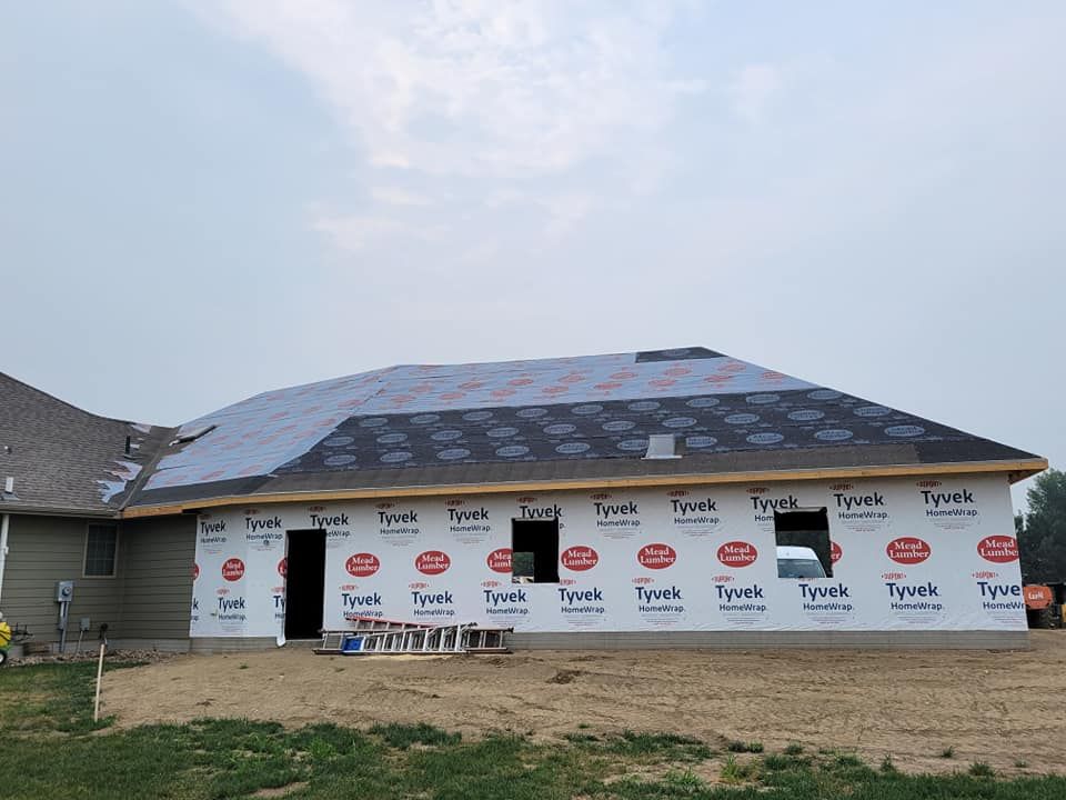 Partially built house with wrapped exterior walls and a roof under construction under a cloudy sky
