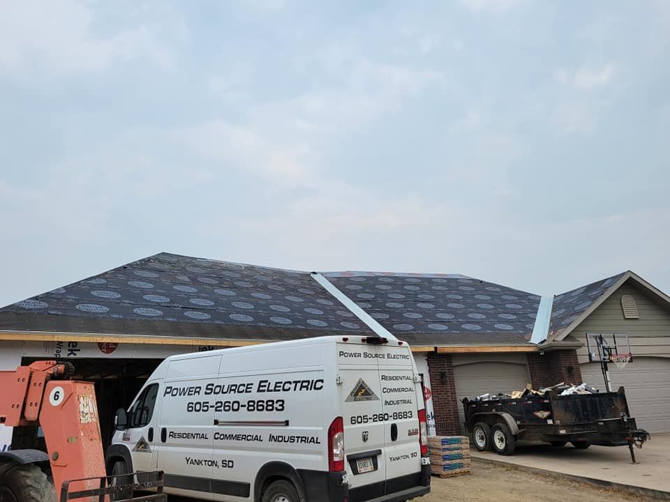 Roofers working on a house with new dark shingles and a utility trailer in the driveway