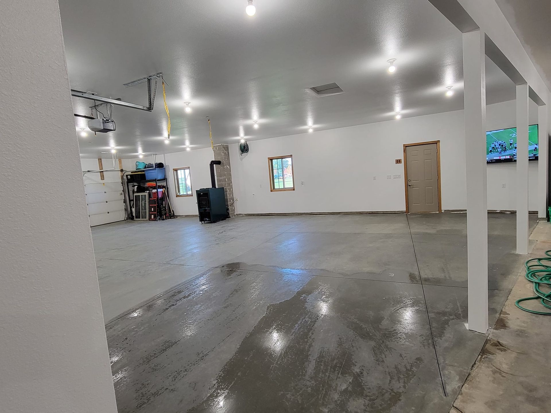 Empty unfinished indoor room with wet concrete floor, white walls, ceiling lights, and a doorway.