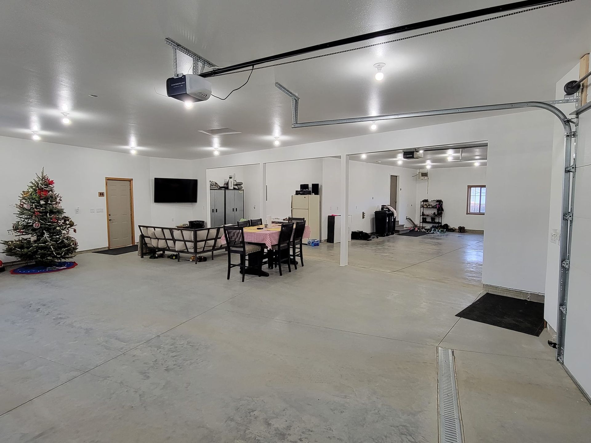 Large garage or workshop interior with Christmas tree, tables and chairs, and a wall-mounted TV
