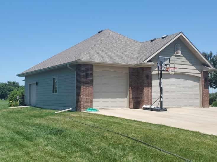Suburban house with gray roof, brick accents, garage, and a portable basketball hoop on the driveway