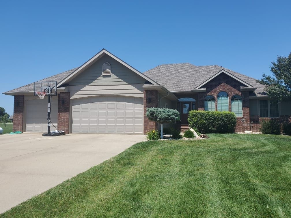 Suburban brick house with a two-car garage, front lawn, and concrete driveway under a clear blue sky