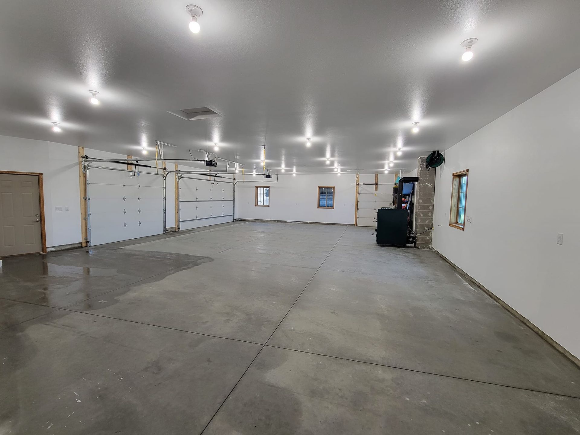 Large empty garage with concrete floor, white walls, overhead lights, and a garage door at the back