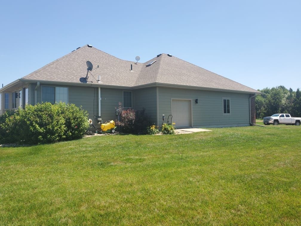 Single-story gray house with a large green lawn and shrubs under a clear sky