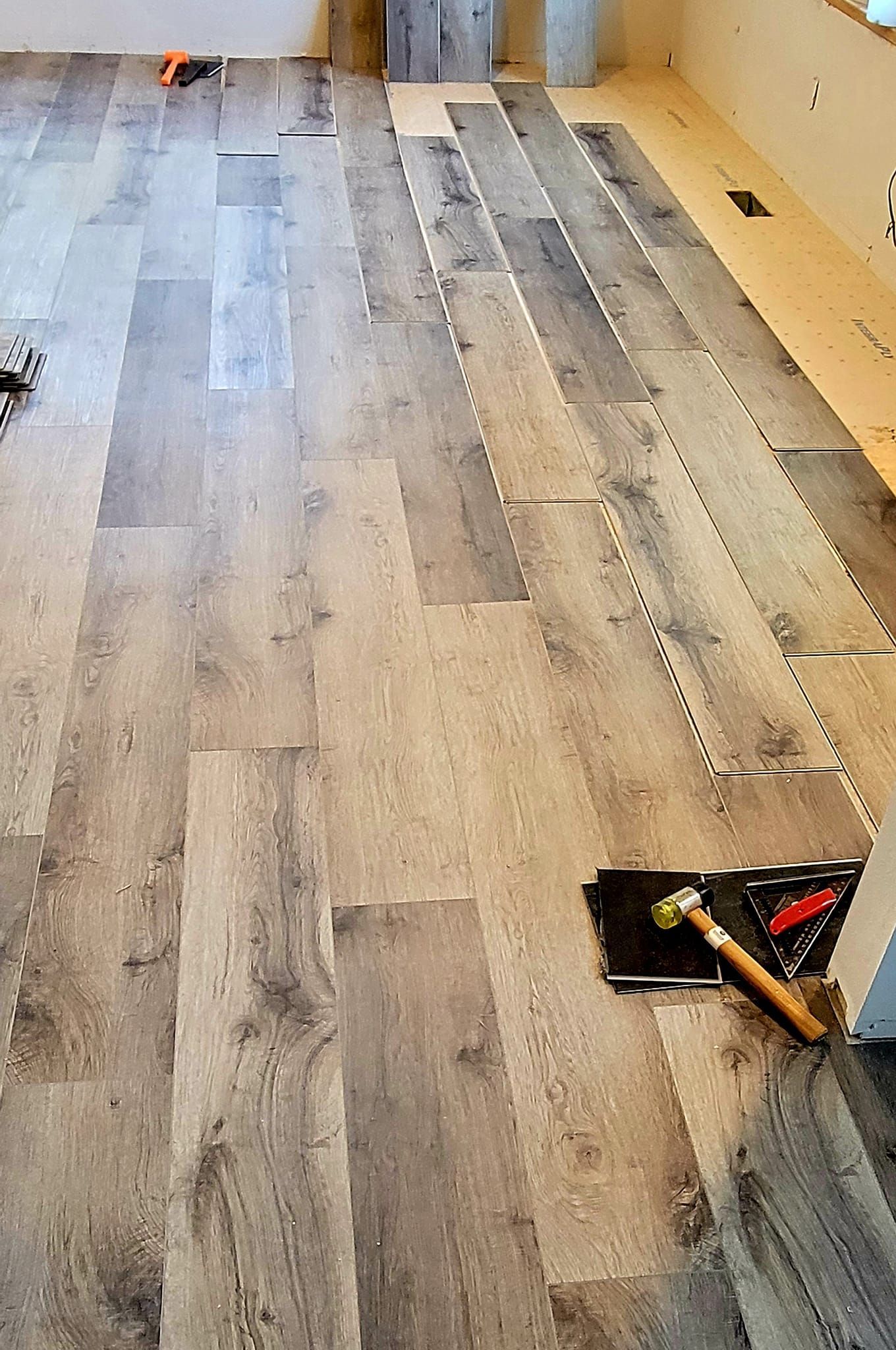 Partially installed gray wood flooring in a room, with tools visible near the doorway