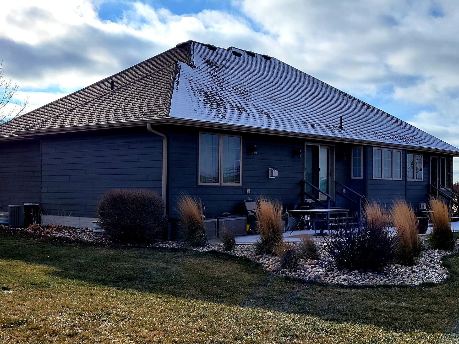 Blue house with a steep metal roof and front porch, surrounded by shrubs and a grassy yard