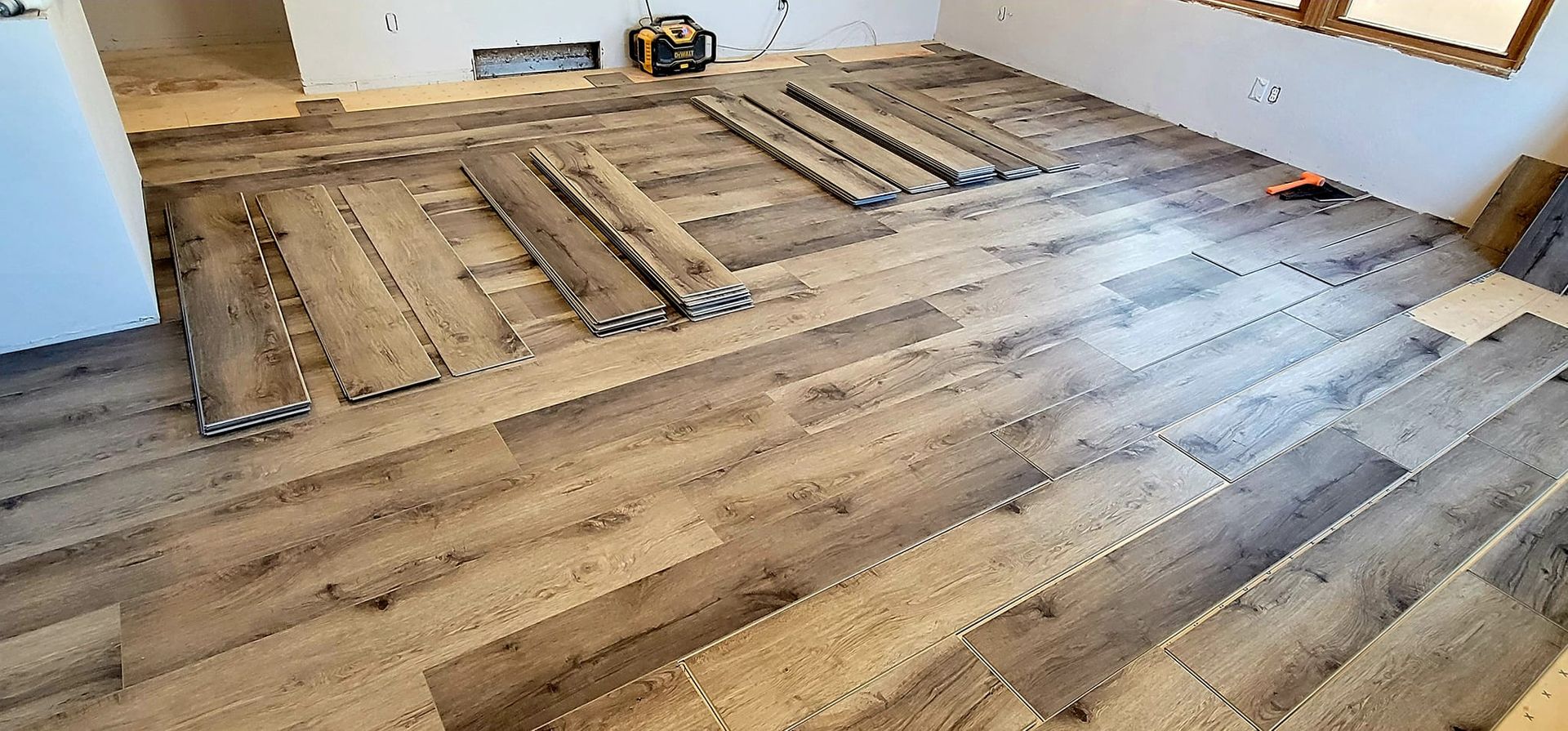 Partially installed wood flooring in a bright room with boards laid out across the floor