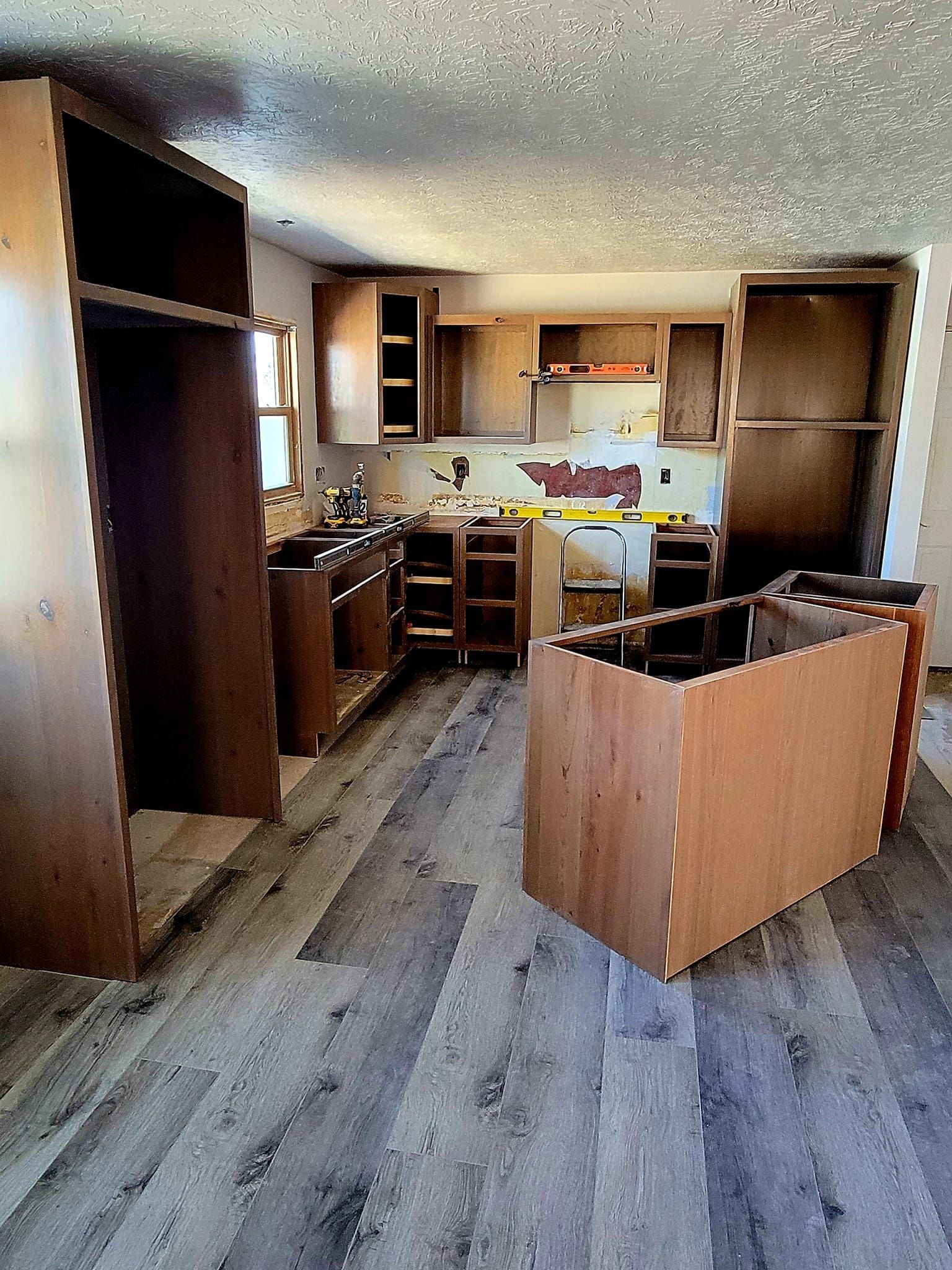 Partially renovated kitchen with unfinished wood cabinets, bare floorboards, and a small island in the center