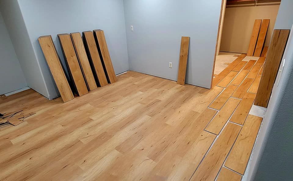 Empty room with light wood flooring, stacked boards, and wood planks laid along the right side