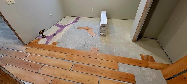 Partially renovated room with exposed floorboards, patchy subfloor, and a small white object near the center.
