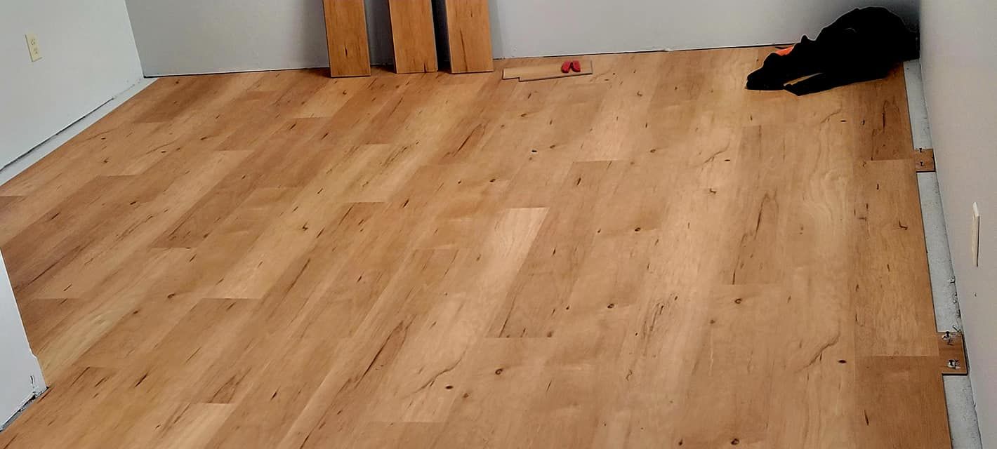 Empty wooden-floored room with white walls and a dark cat curled in the back-right corner.
