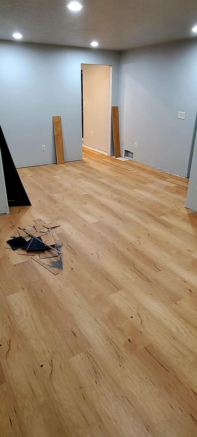 Empty room with light wood flooring, gray walls, and scattered construction materials near an open doorway