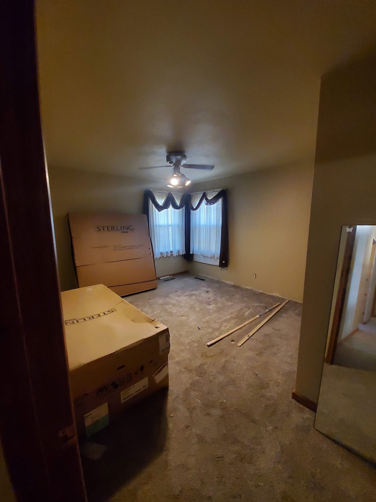 Empty bedroom with carpet, ceiling fan, dresser, and a bed frame near a window with curtains.