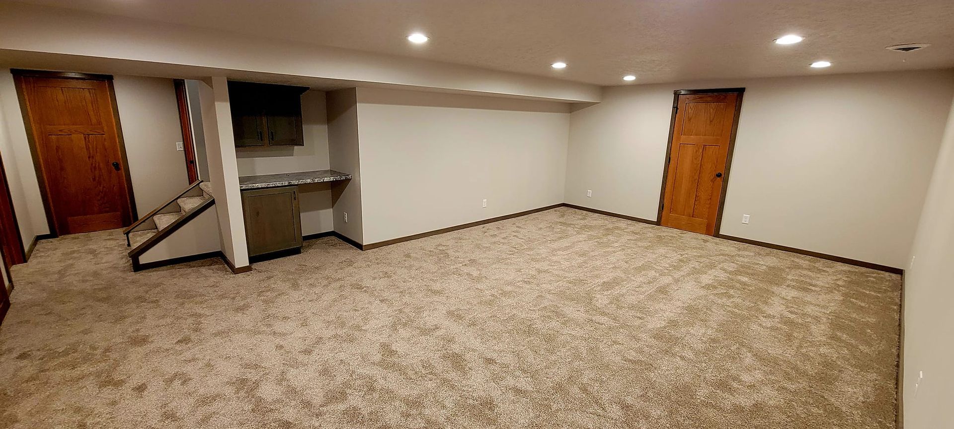 Empty carpeted basement room with recessed lights, wood doors, and a small fireplace alcove