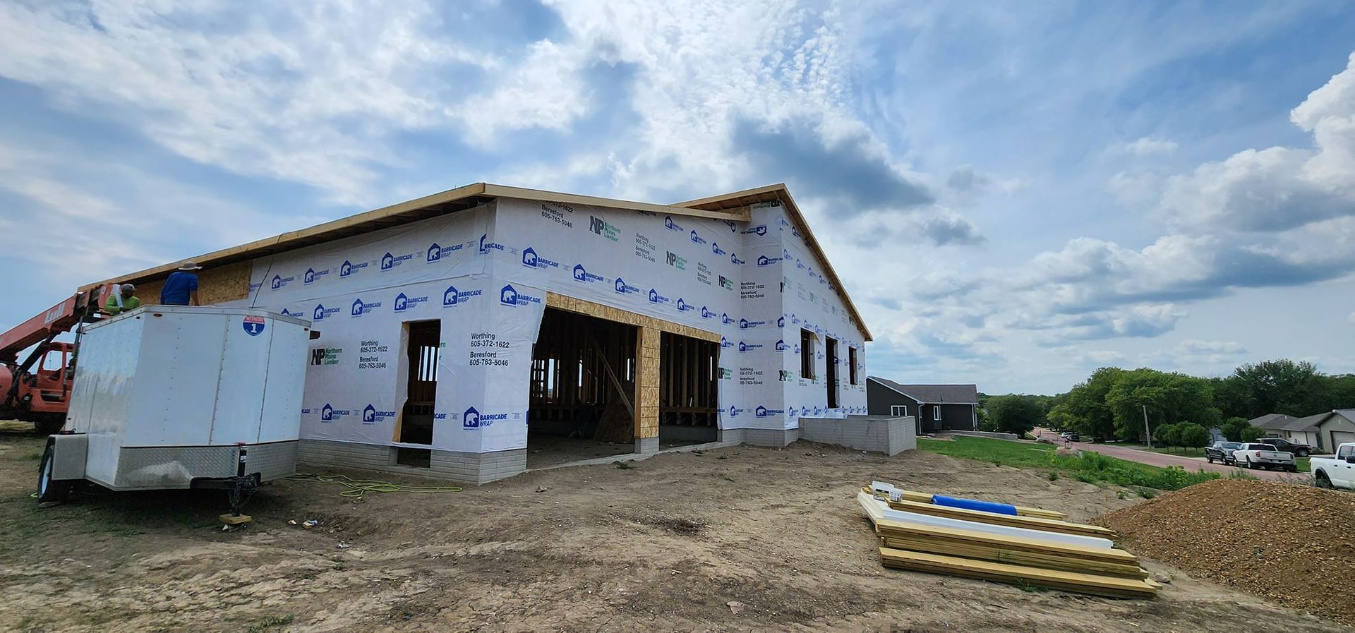 Partially built house wrapped in white housewrap on a dirt lot under a cloudy sky