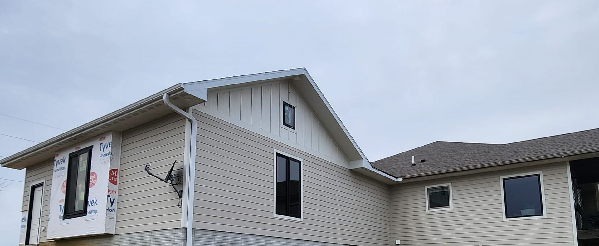 Partially built house exterior with white siding, black-framed windows, and roof under cloudy sky