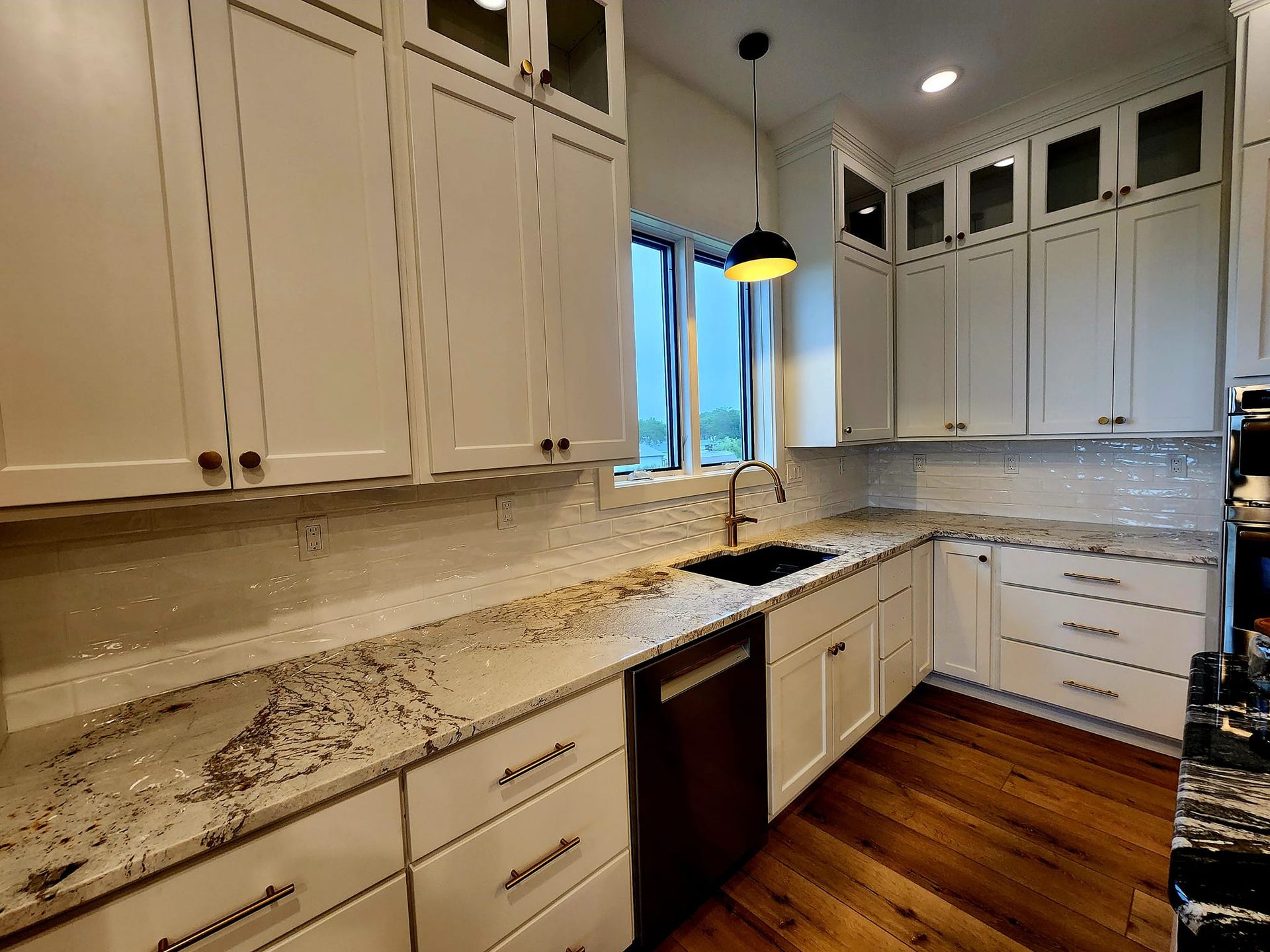 Modern kitchen with white cabinets, granite countertops, stainless dishwasher, and wood flooring
