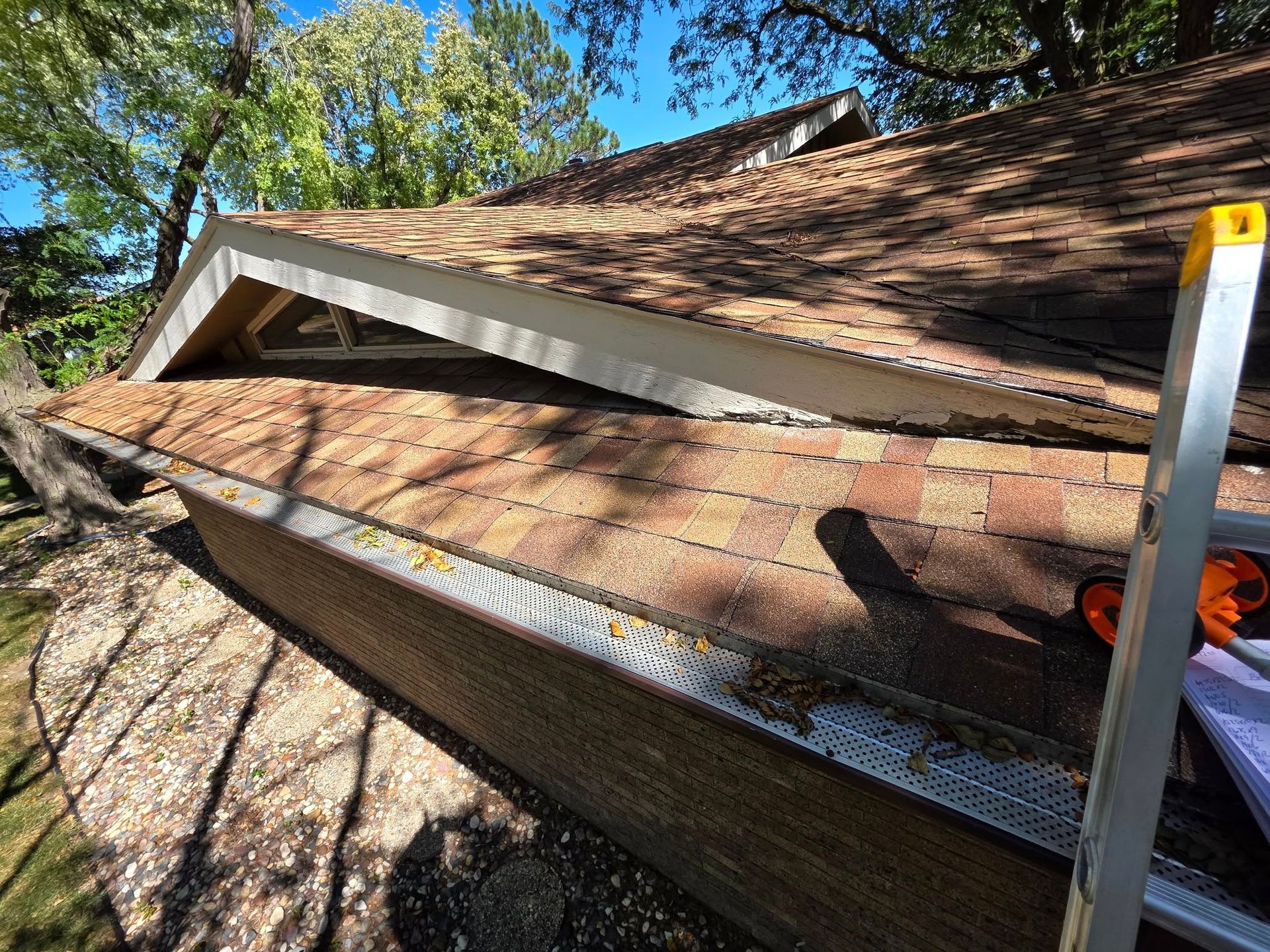 Roof shingles and gutter with a ladder leaning against a house in daylight