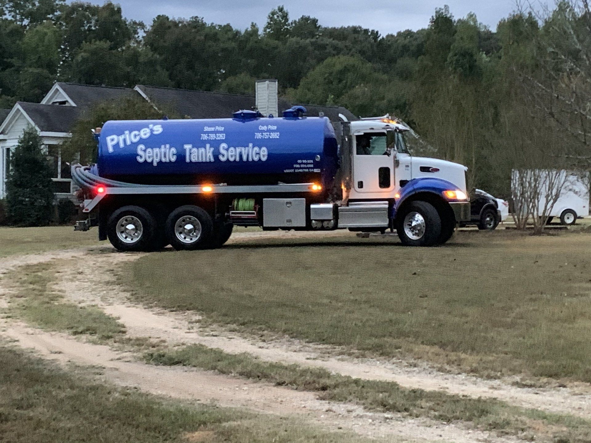 Septic Tank Service truck parked on a grassy dirt drive beside trees and houses.