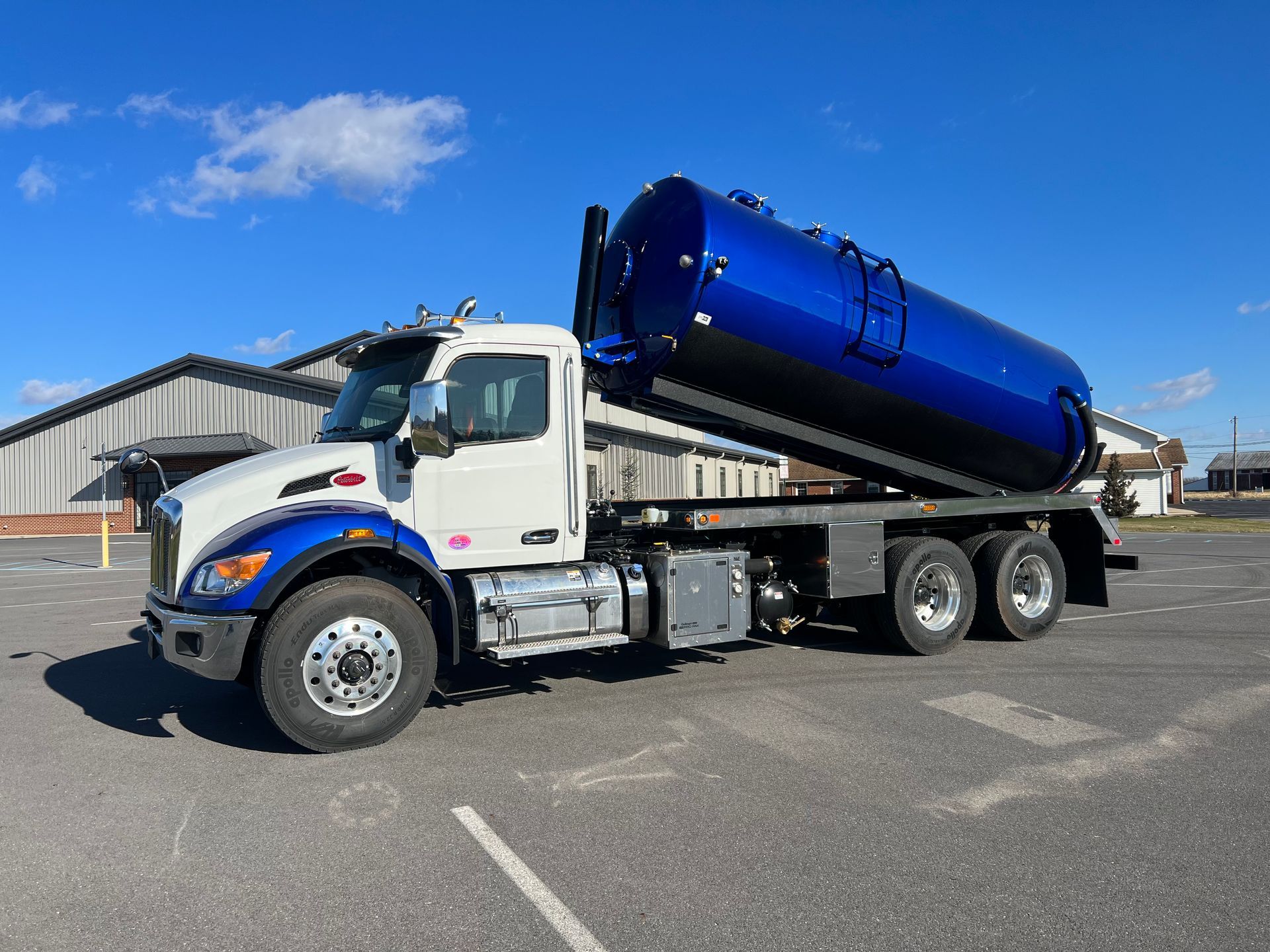 Blue and white septic truck on a paved lot, under a blue sky.